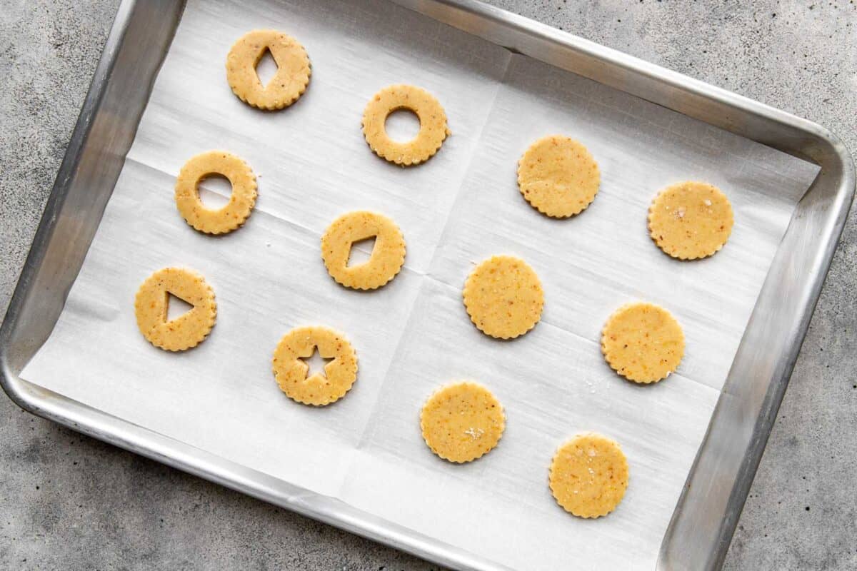 Unbaked linzer cookie dough cut outs on a parchment paper lined baking sheet.
