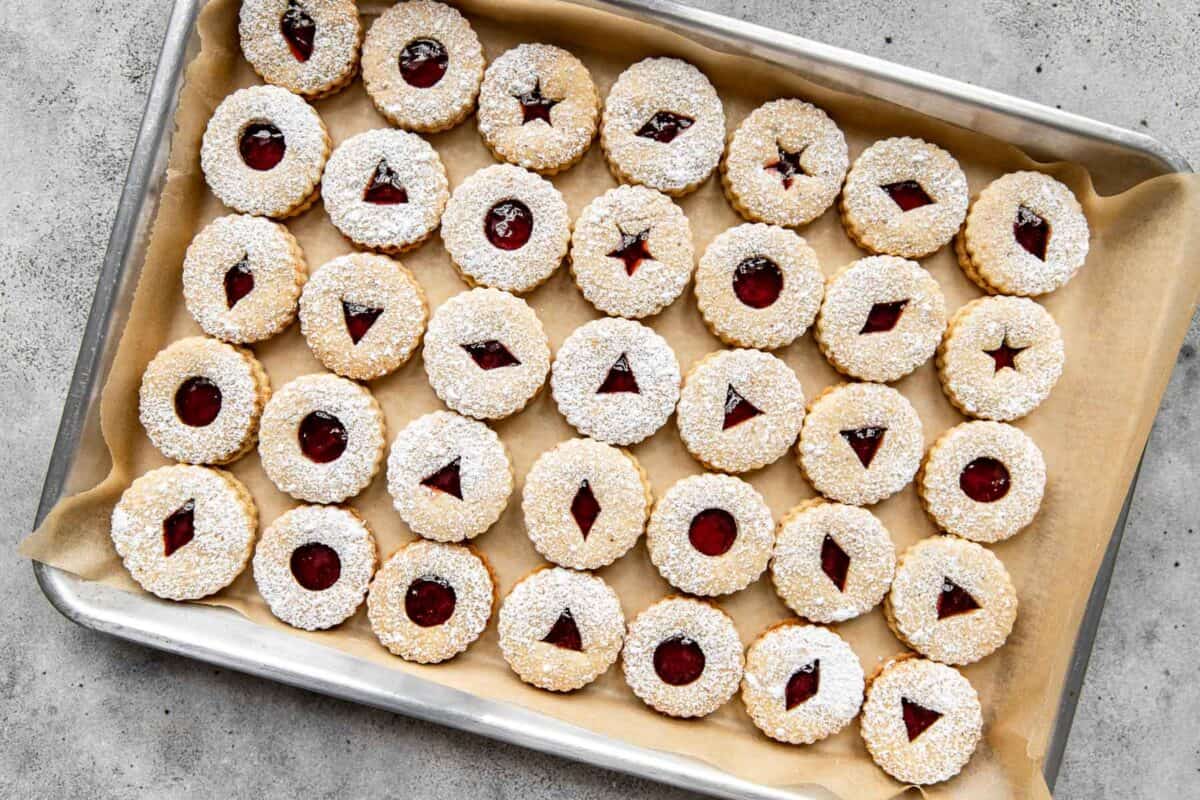 Filled and dusted linzer cookies on a parchment-lined baking sheet. 