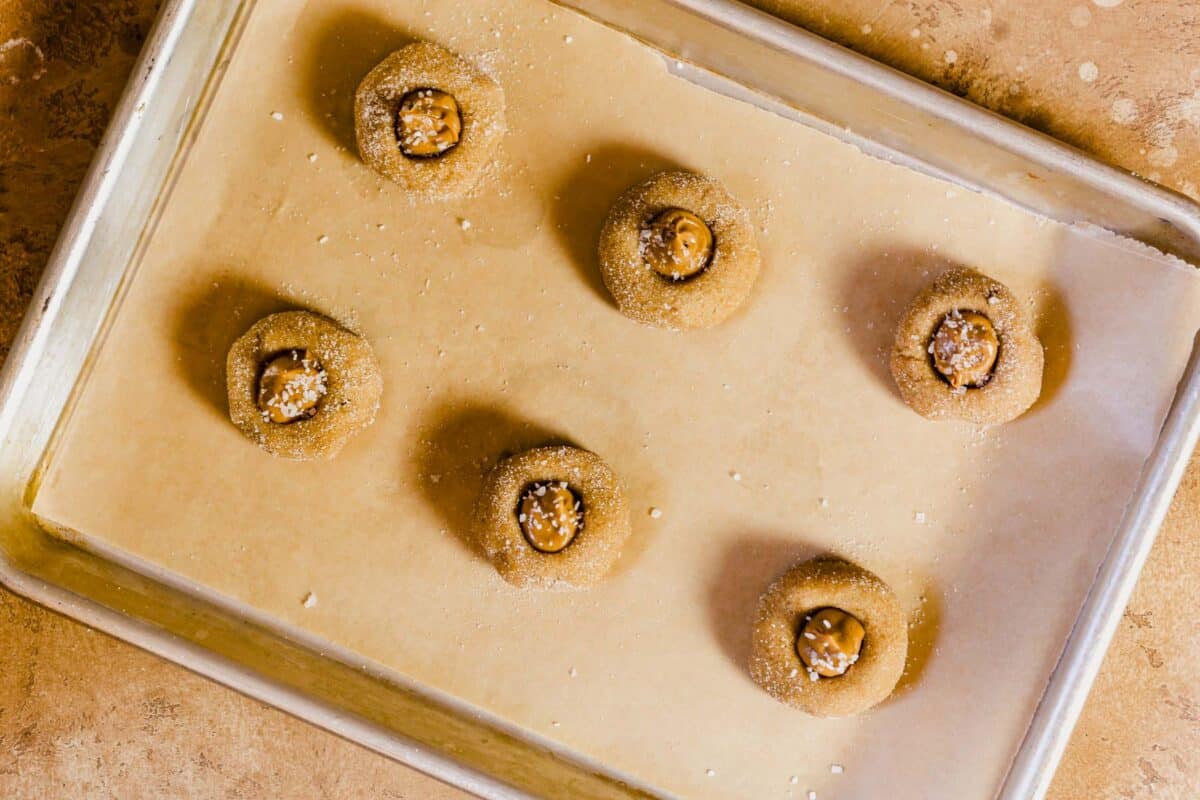 Peanut butter cookie dough balls filled wit peanut butter on a parchment lined baking sheet.