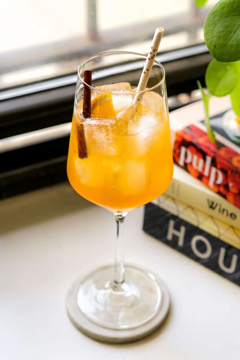 Amaretto Spritz in a wine glass garnished with a cinnamon stick and orange wedge.