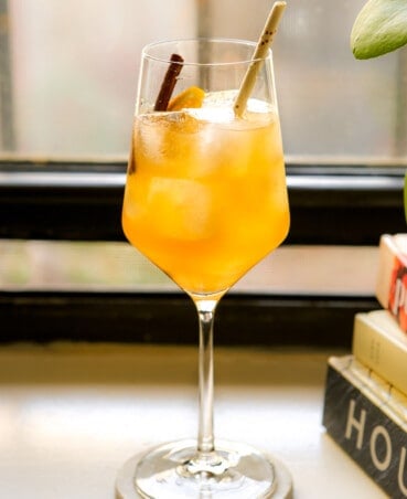 Amaretto Spritz in a wine glass garnished with a cinnamon stick and orange wedge.