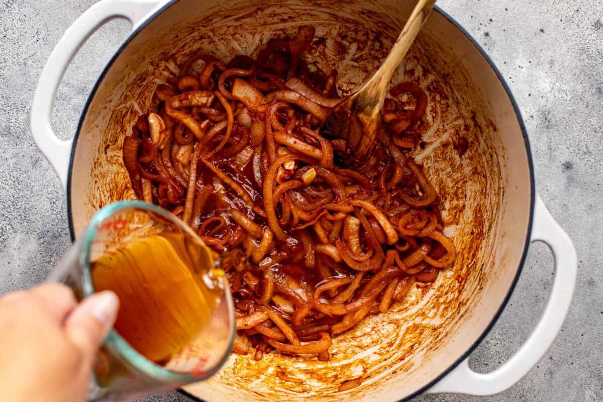 saucy caramelized onions in a large Dutch oven with broth being poured in.