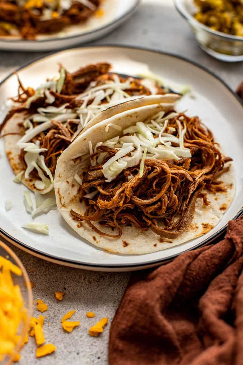 Shredded beef tacos on a plate topped with shredded cabbage.