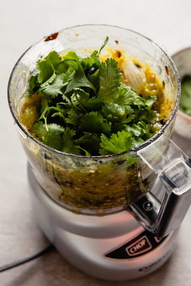 Fresh cilantro piled into a food processor full of charred onion and tomatillos.