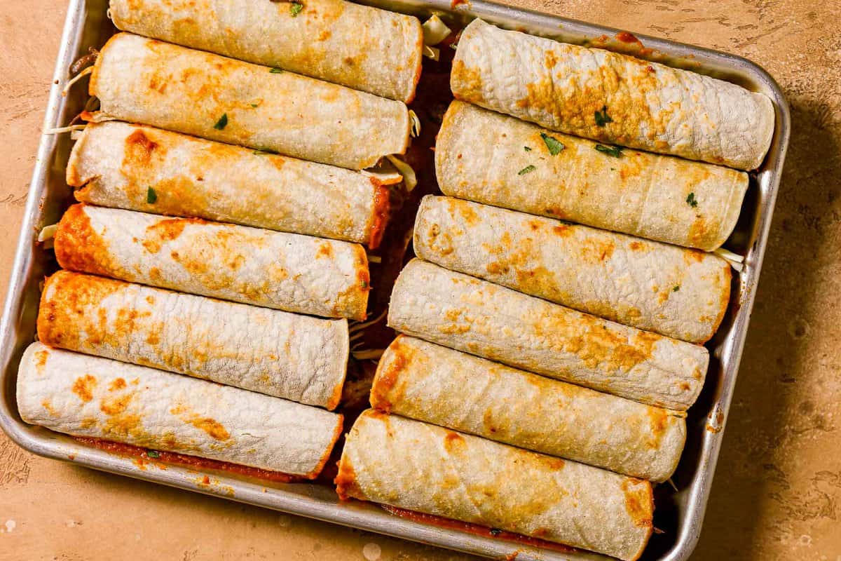 a small sheetpan filled with unbaked shredded beef enchiladas.