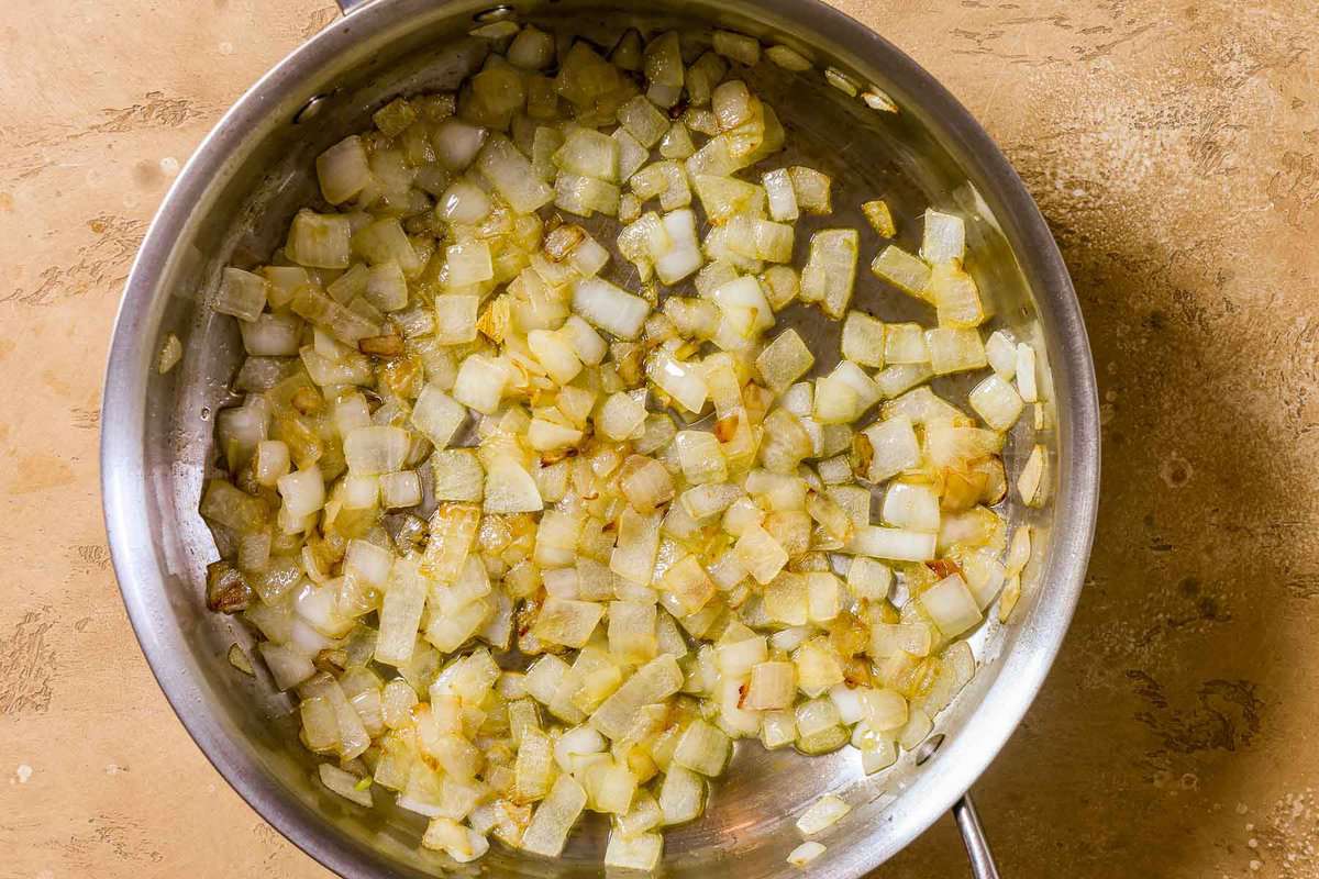 A sauté pan with chopped onions cooking in olive oil.