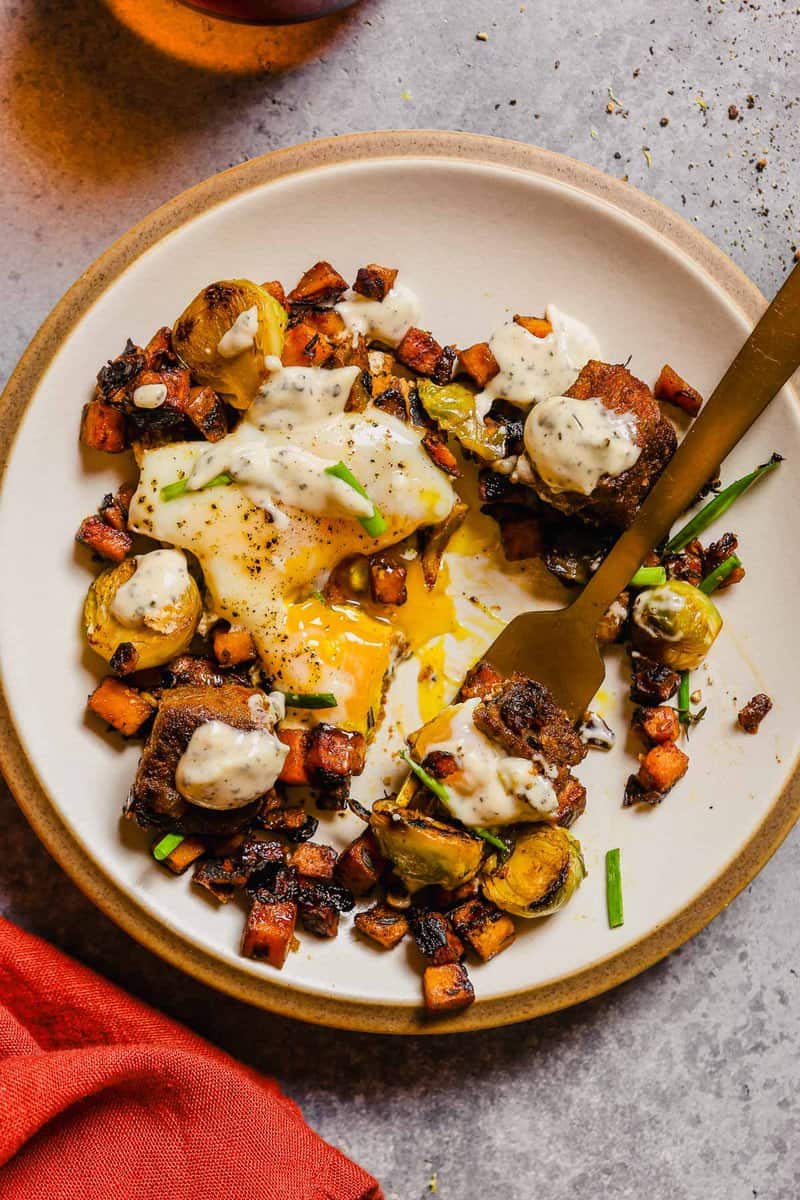 sweet potato and steak breakfast hash scooped onto a white plate with fresh chives and a gold fork.