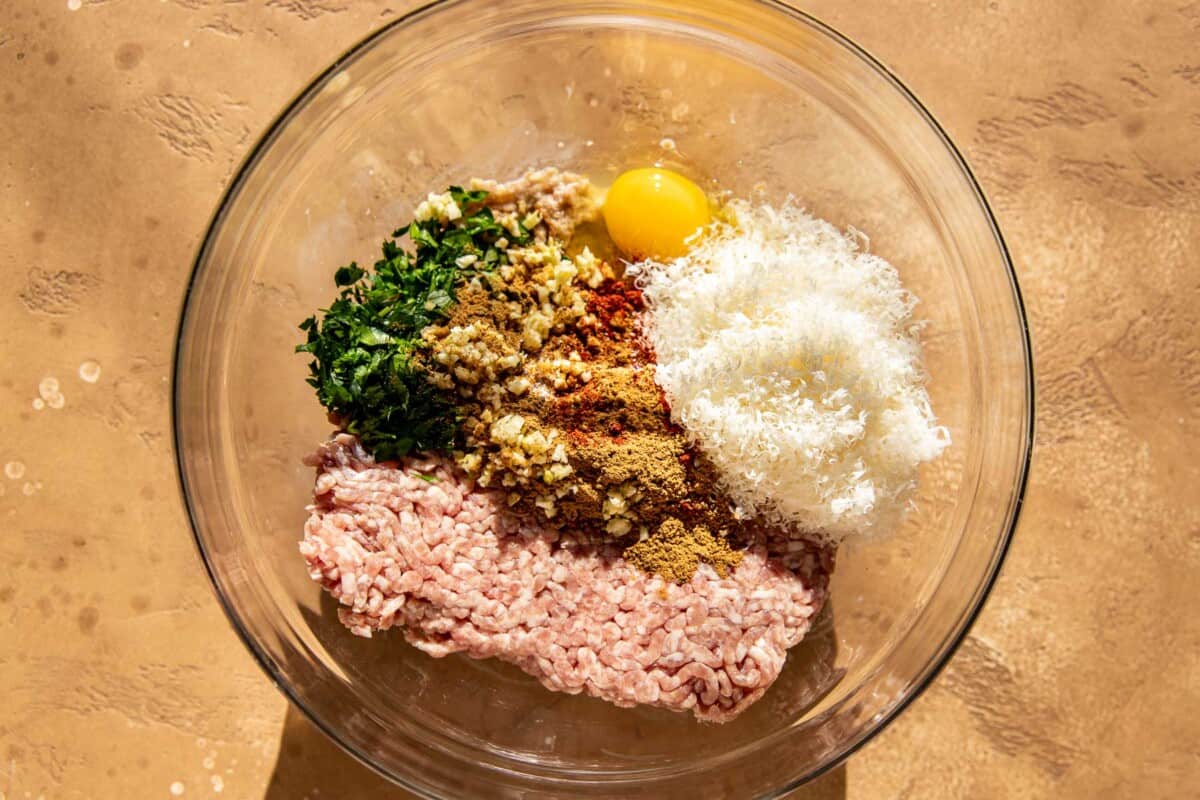 Ground pork, grated cheese, egg, parsley, spices and garlic in a mixing bowl.