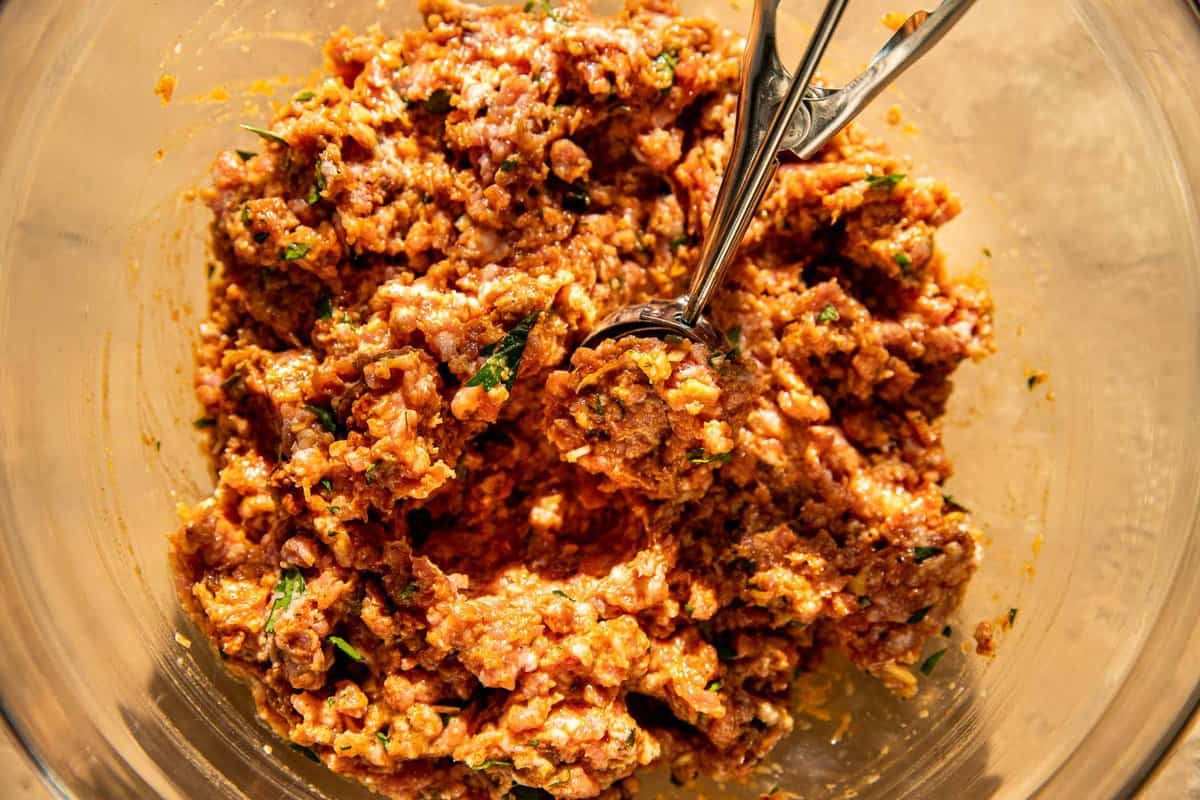 Spiced ground pork in a glass bowl with a scoop in it.