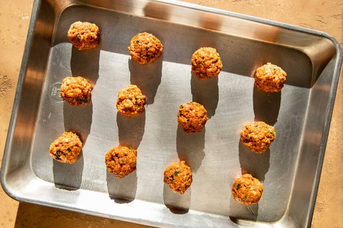 Uncooked meatballs arranged on a baking sheet.