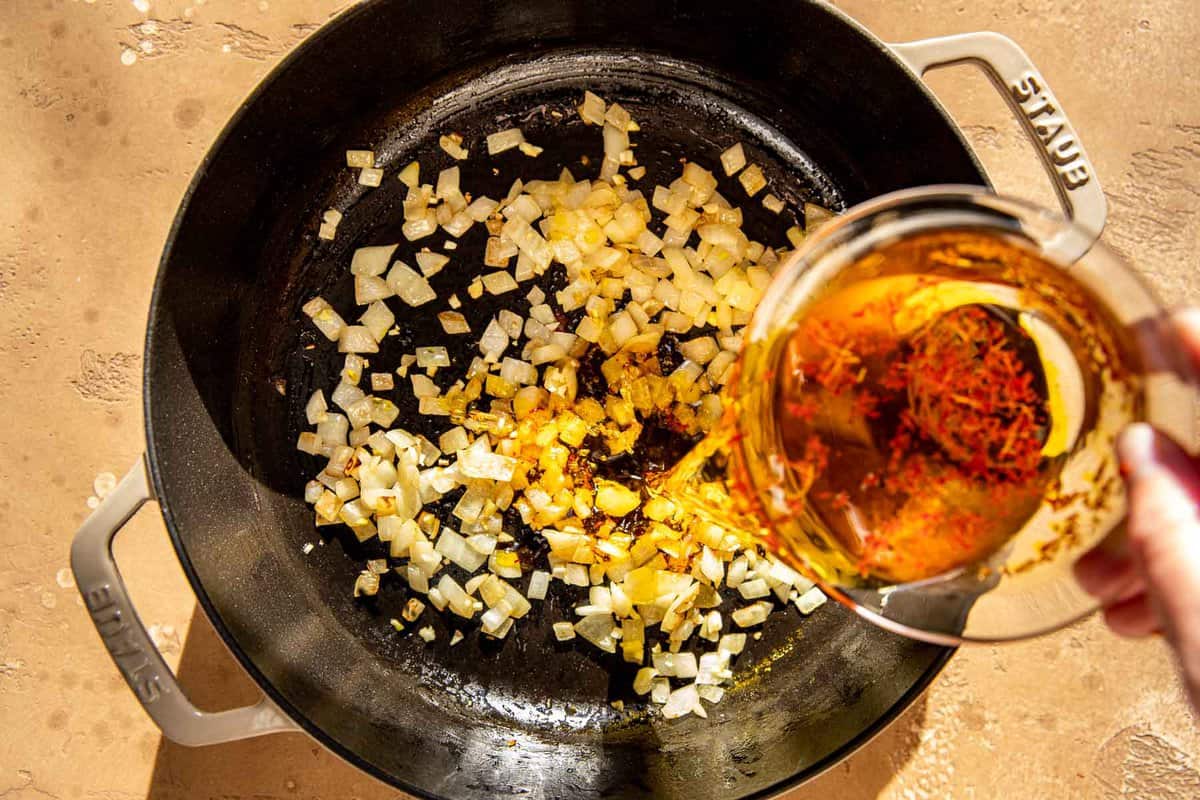 Sherry being poured into a skillet with diced sauteed onions.