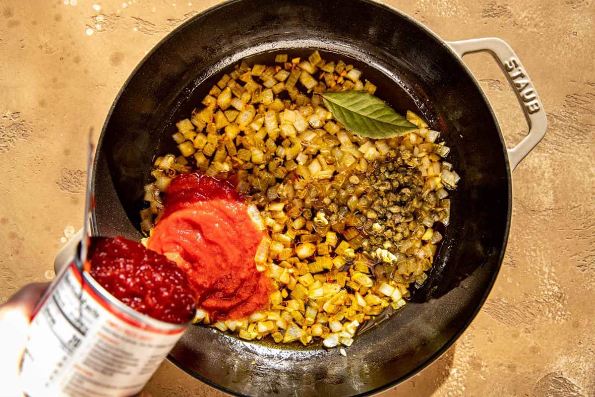 canned crushed tomatoes getting poured into a cast-iron skillet with cooked onions in it