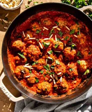 Pork spanish meatballs in a tomato sauce in a large skillet with slivered almonds and chopped parsley sprinkled over top