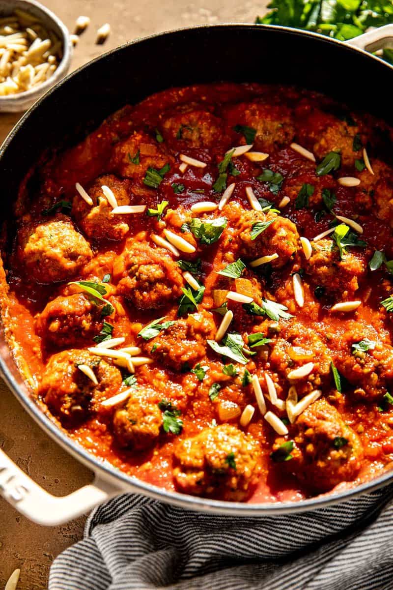 Pork spanish meatballs in a tomato sauce in a large skillet with slivered almonds and chopped parsley sprinkled over top