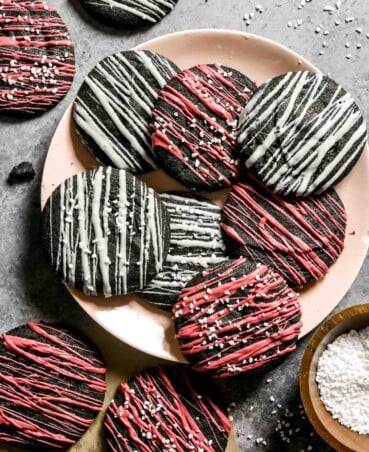 Chewy black sesame cookies with white chocolate and ruby chocolate drizzled over top stacked on a light pink plate.