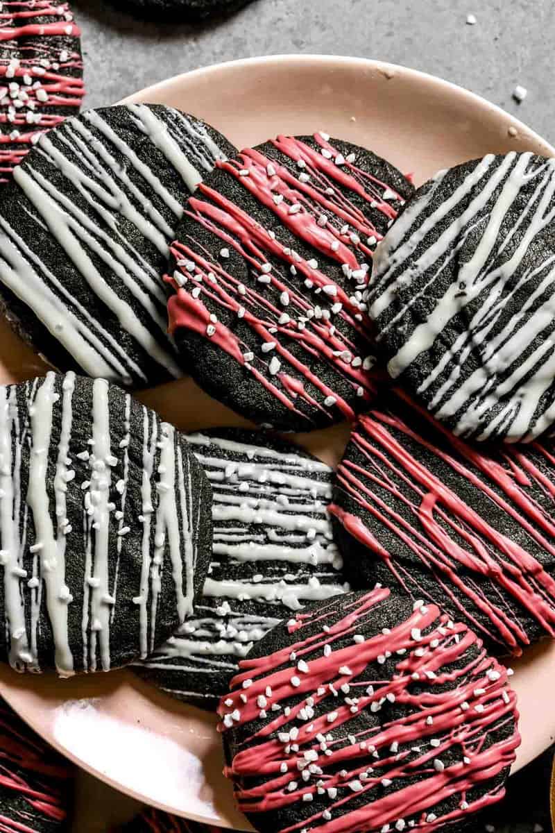 Chewy black sesame cookies with white chocolate and ruby chocolate drizzled over top set on a light pink plate.