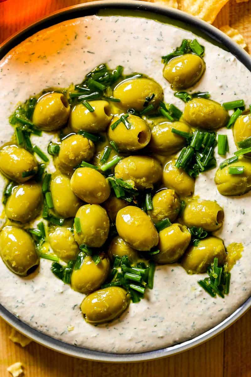Olives and chives on top of a creamy salmon dip on a plate.
