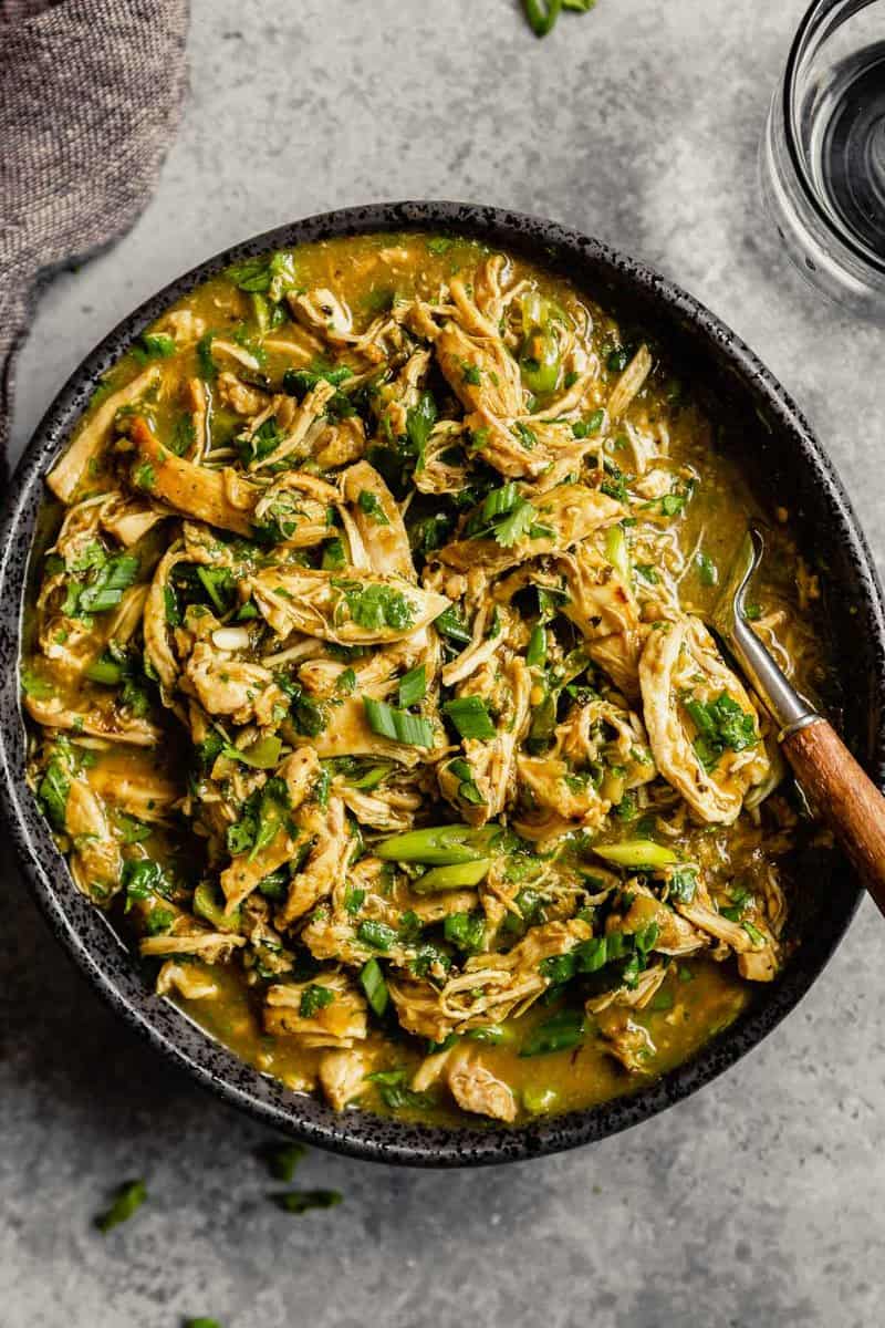 Shredded salsa verde chicken in a large black serving bowl with a spoon set in it.