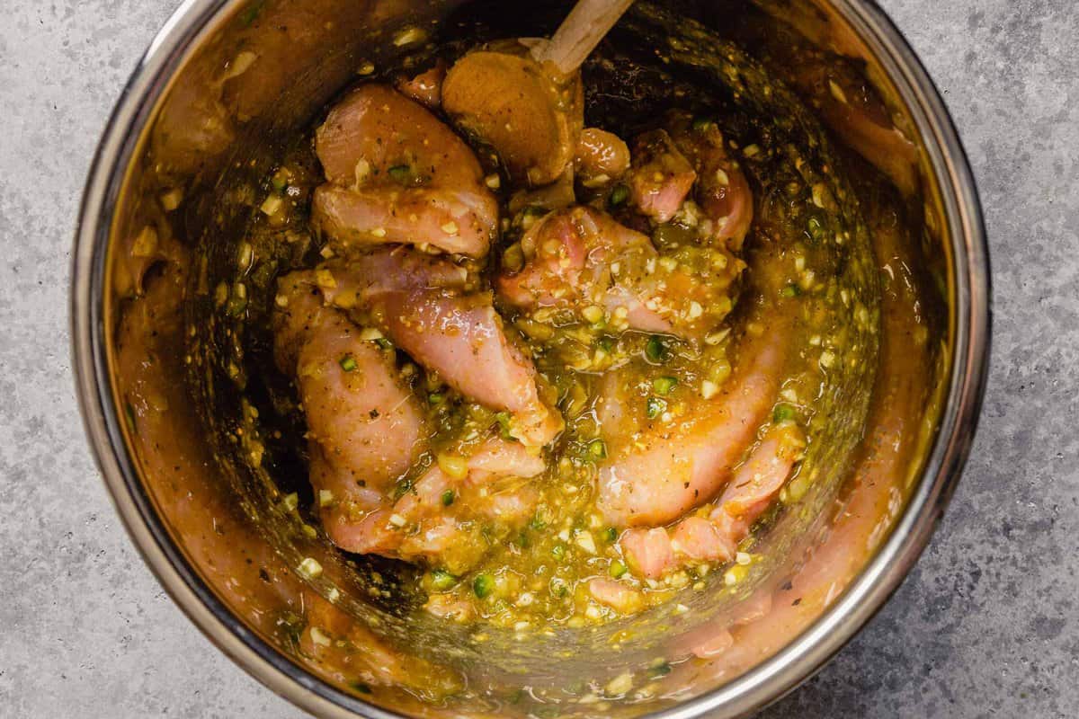 Raw chicken breast and chicken thighs in a pot covered in salsa verde.