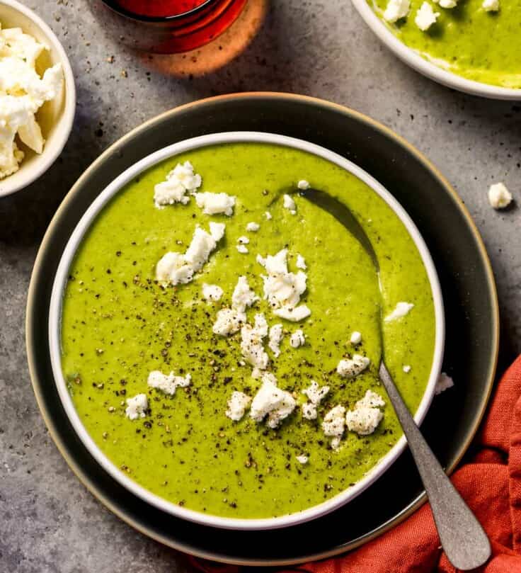 Vibrant green broccoli and feta soup in a shallow white bowl with crumbled feta over top
