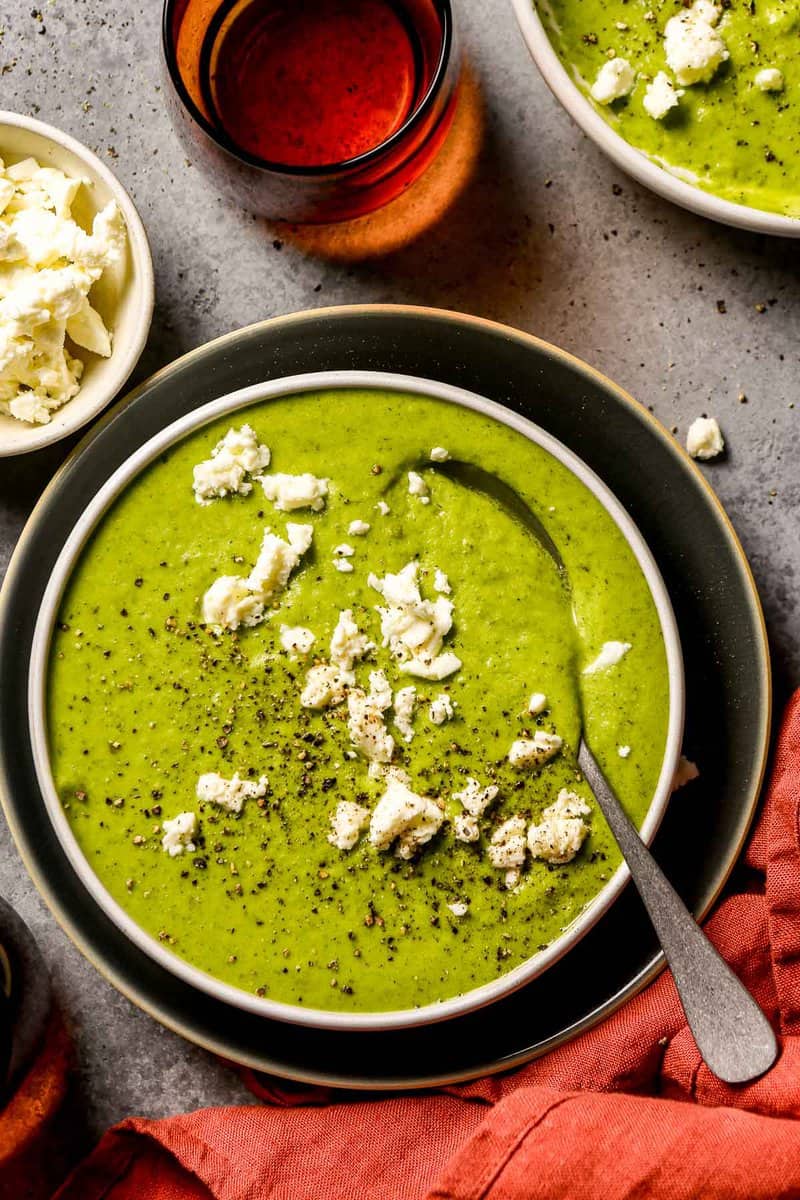 Vibrant green broccoli and feta soup in a shallow white bowl with crumbled feta over top