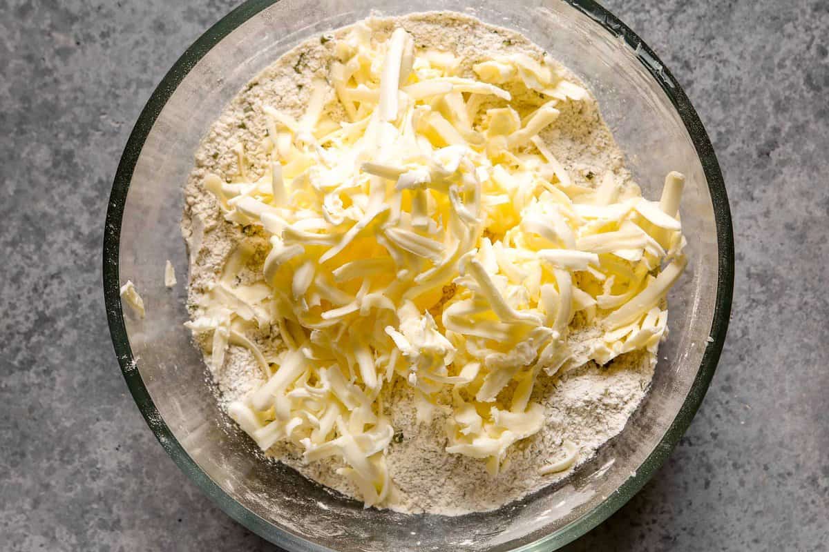 Shredded butter added to a glass mixing bowl with a flour mixture in it.