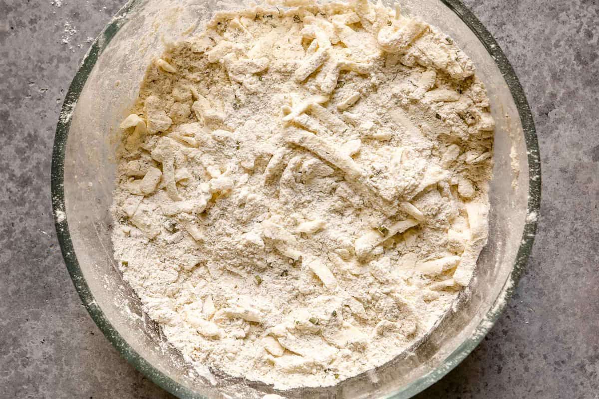 Flour and shredded butter tossed together in a glass mixing bowl.