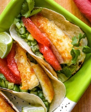 Fish tacos with cilantro, cucumber and grapefruit in a metal tray.