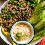 Large white serving bowl filled with meat salad, a small bowl of rice and lettuce leaves.