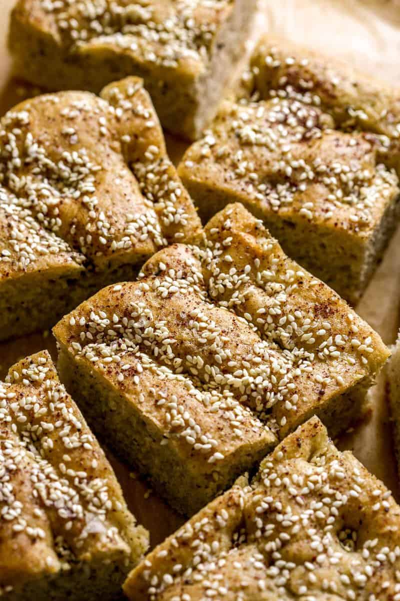 large pieces of focaccia bread on parchment paper. Bread topped with sesame seeds, salt and sumac.