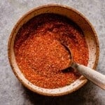 Cajun seasoning blend in a small bowl set on a counter with a measuring spoon set in it.