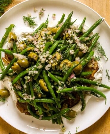 Green beans and smashed potatoes piled onto a larger serving platter with a swipe of greek yogurt underneath.