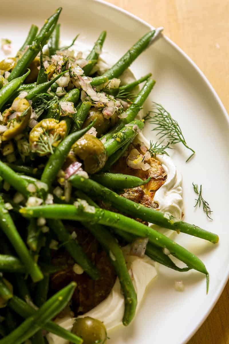 Smashed potatoes and green beans on a bed of greek yogurt with dill, shallots and olives intermixed. 