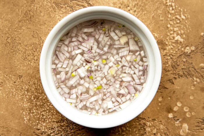MInced shallots in a small white bowl with water.