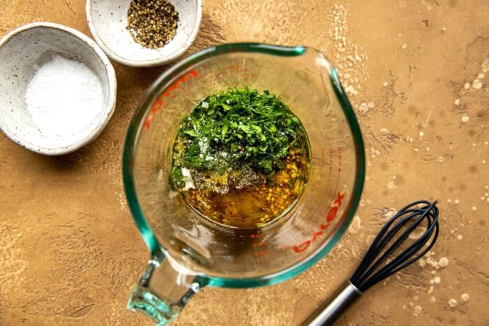 herbs, oil, vinegar, mustard and shallot in a liquid measuring cup. 