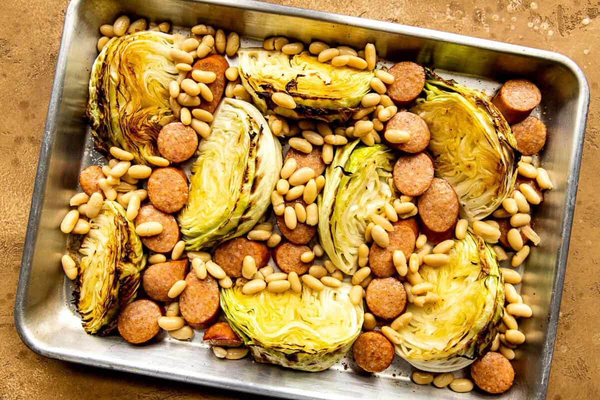Cabbage, sausage and white beans on a baking sheet.