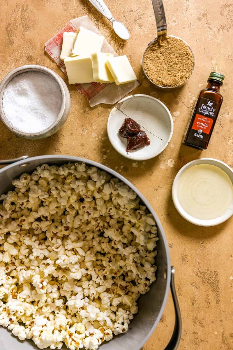 Butter, vanilla, brown sugar, gochujang, corn syrup, popcorn and salt set out on a counter in preparation for making caramel corn.