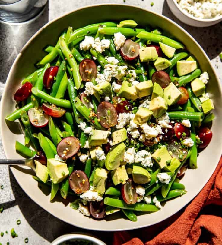 Cold green bean salad in a large serving bowl with green beans, grapes, avocado and blue cheese.