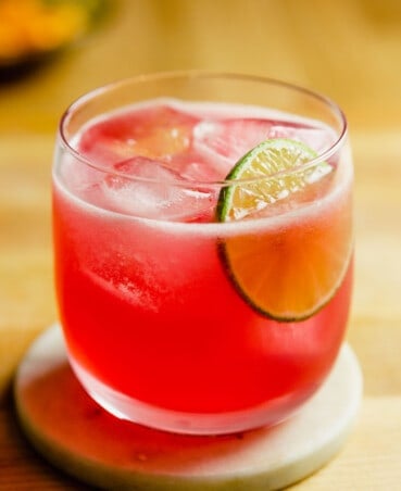 Vibrant pink hibiscus margarita in a rocks glass with a lime wheel as garnish.