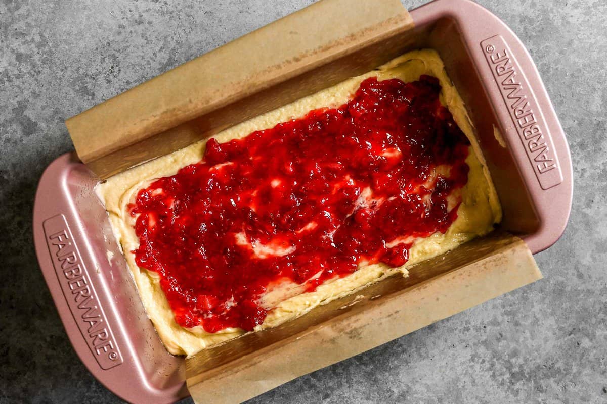 Pound cake batter in a loaf pan topped with a layer of strawberry jam.