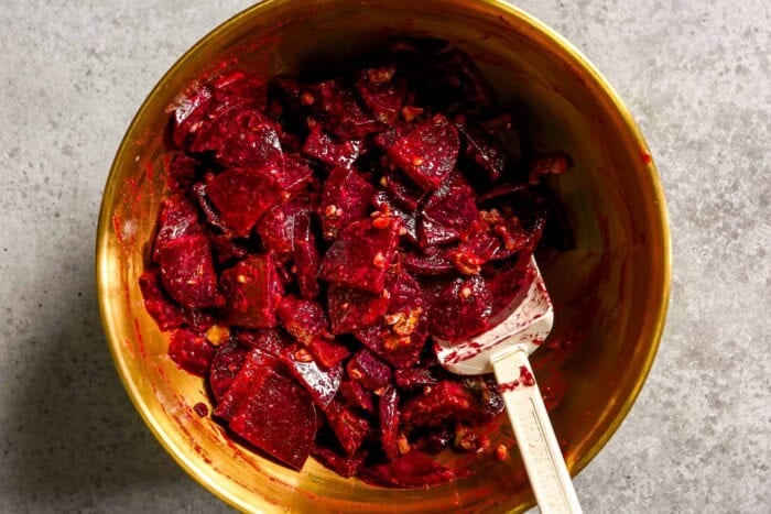 Roasted beets tossed in a walnut vinaigrette in a gold mixing bowl with a white rubber spatula.