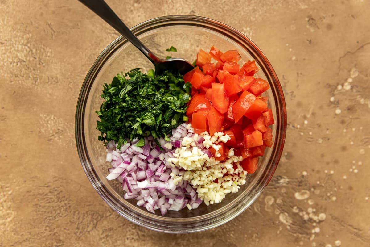 Diced tomatoes, chopped jalapeno, chopped cilantro, minced garlic and chopped red onion in a small glass mixing bowl with a spoon.
