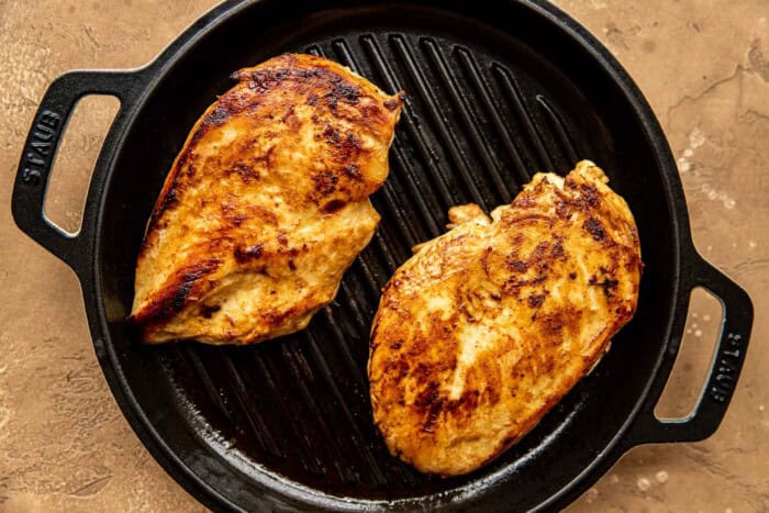 Chicken breasts grilling on a cast-iron grill pan.
