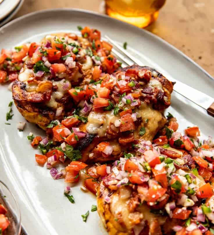 Four grilled chicken breasts topped with cheese, bacon and pico de gallo set on a large platter.