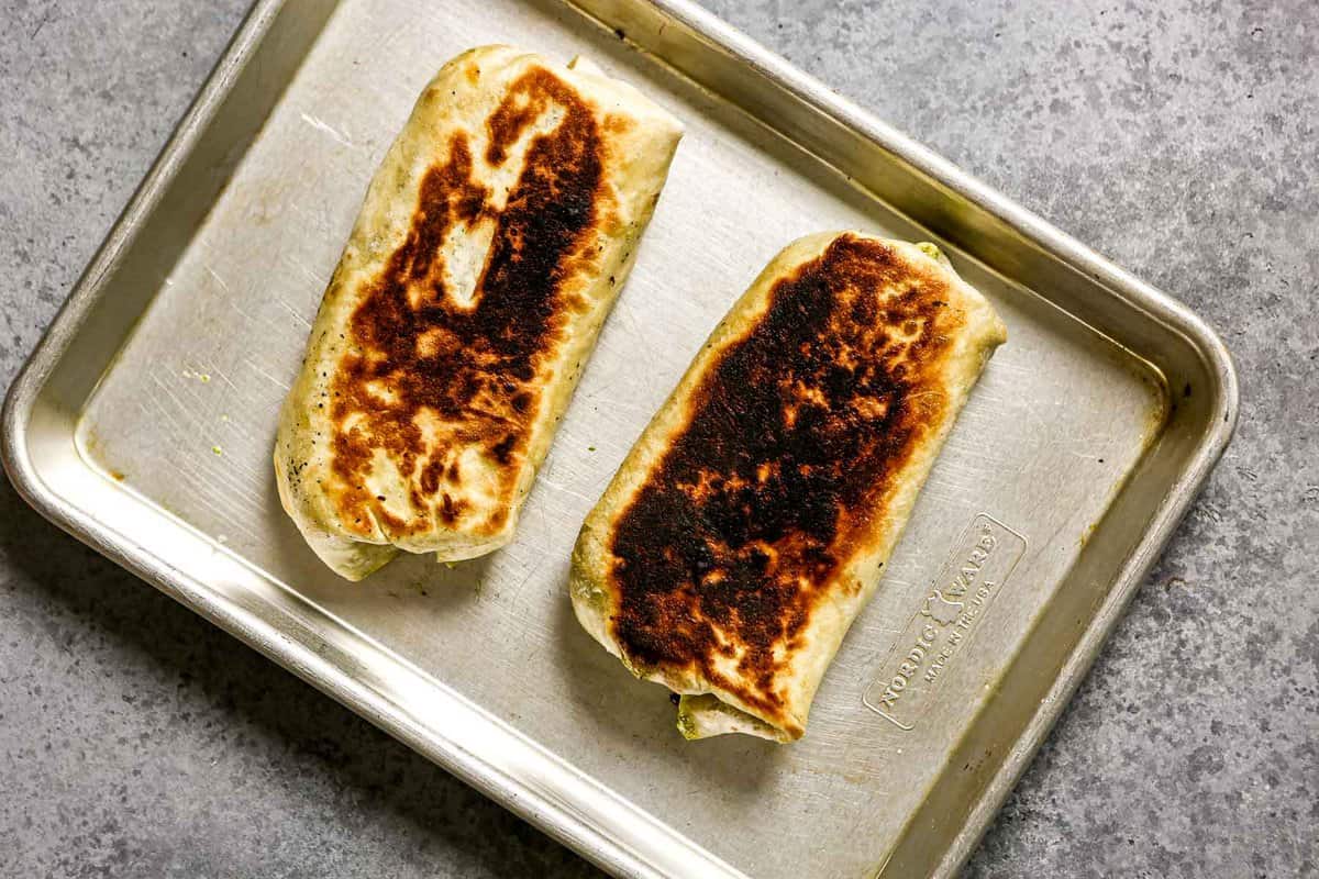 Two pan-fried burritos on a metal sheet pan.