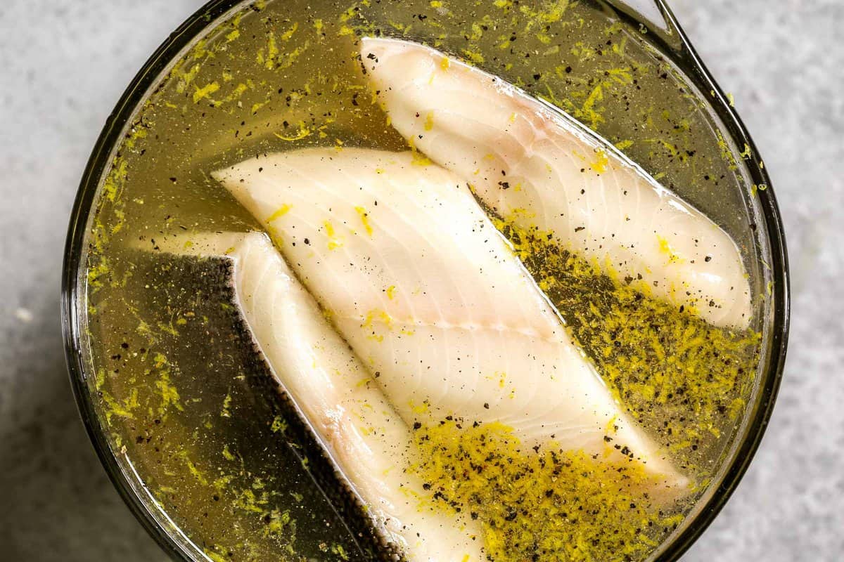 Sablefish fillets in a lemon and black pepper brine in a large glass bowl.