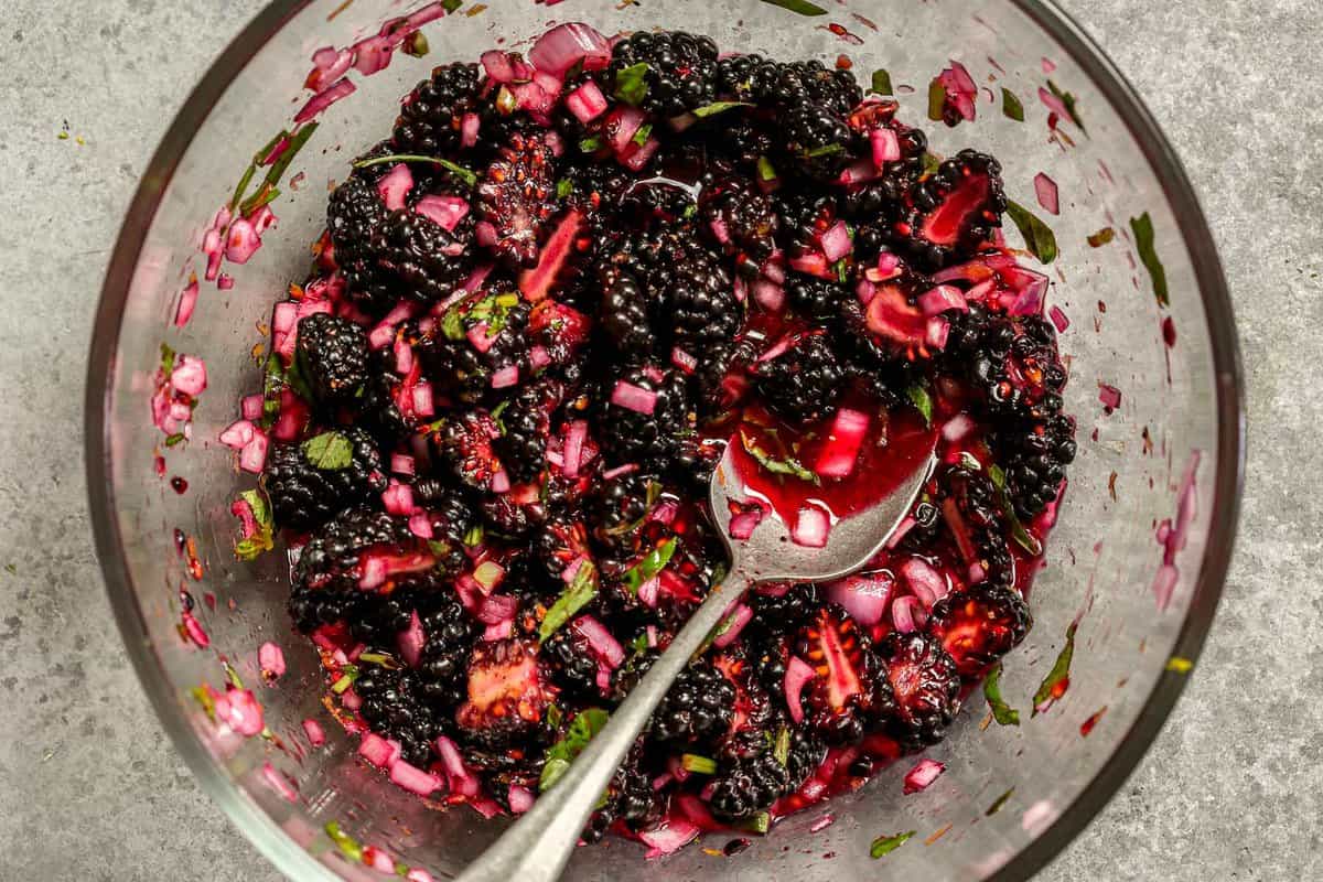 Blackberry relish with minced shallot and chopped basil in a glass mixing bowl with a silver spoon.