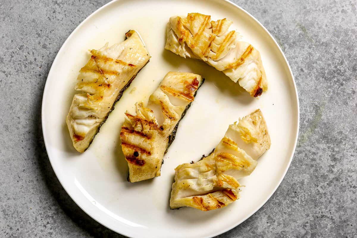 Four grilled sablefish fillets on a large white dinner plate.