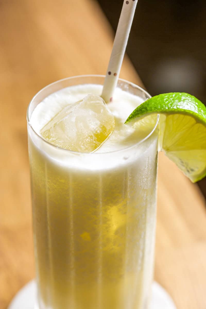 Frozen pina colada in a collins glass filled with ice, garnished with a lime wedge and a straw.