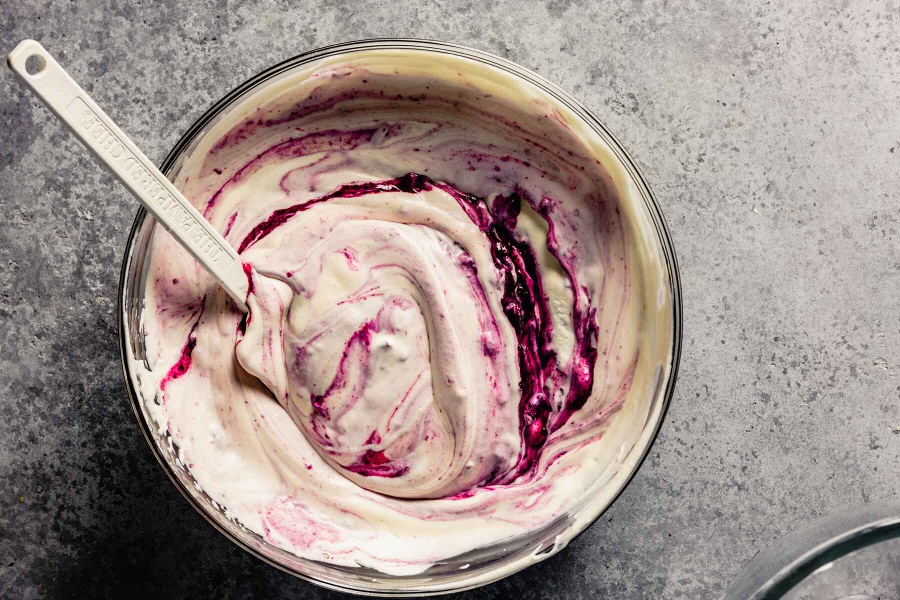 Cherry compote swirled into a creamy mixture in a large glass mixing bowl.